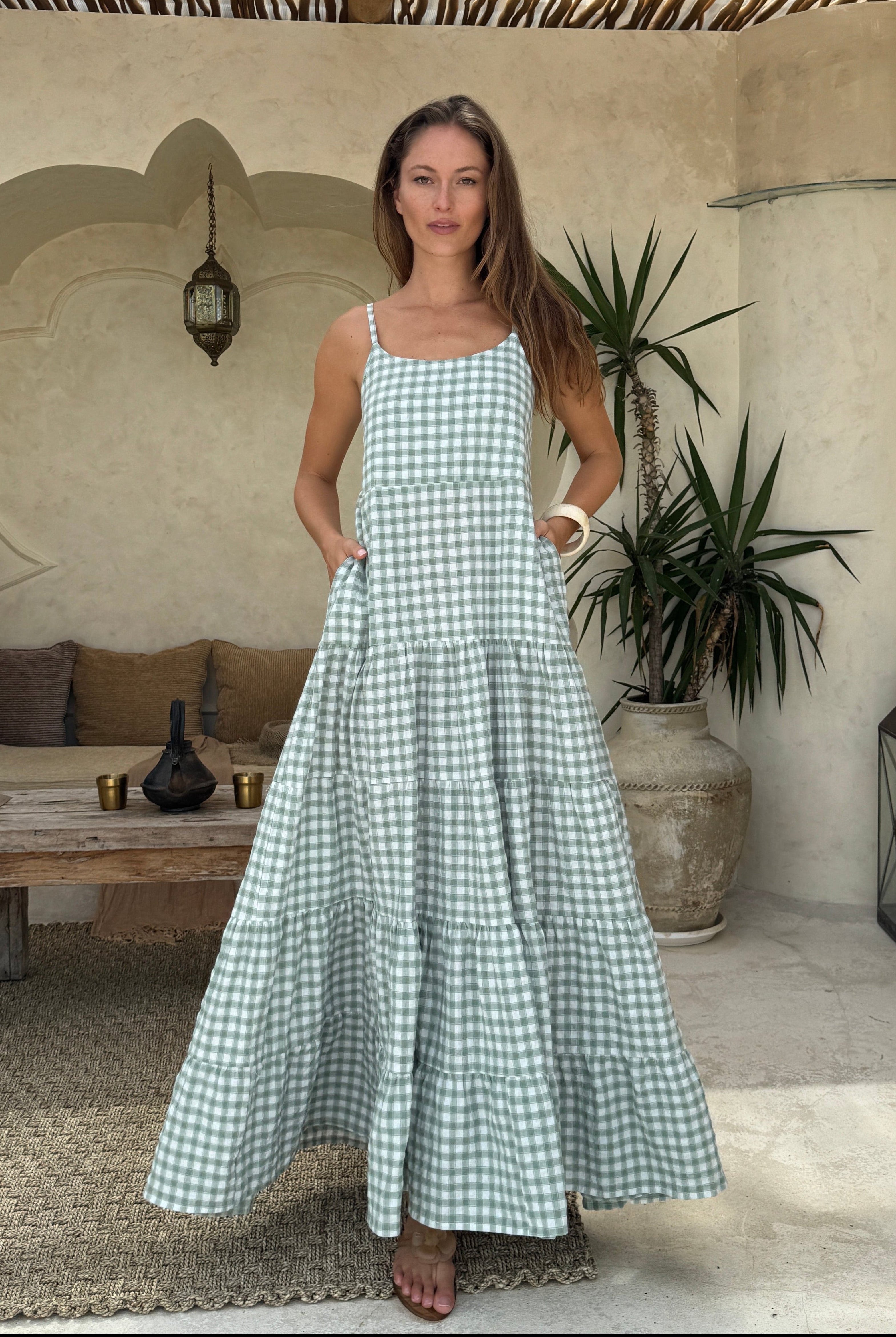 Woman in a green checkered dress standing in a courtyard with plants and lanterns.
