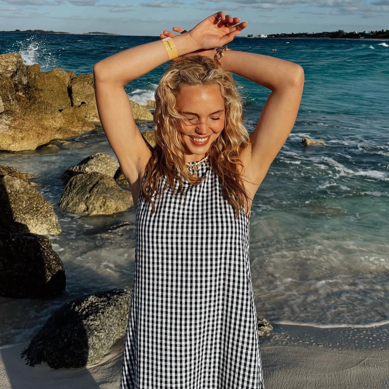 Model Lynden Orr styles a navy blue gingham maxi dress on vacation. Outfit ideas inspired by LynenFruit, Lynden Orr, Beach dresses, outfit inspiration for beach vacations 2026, what to wear on a beach vacation, maxi dresses for the summer 2026, chic easy dresses