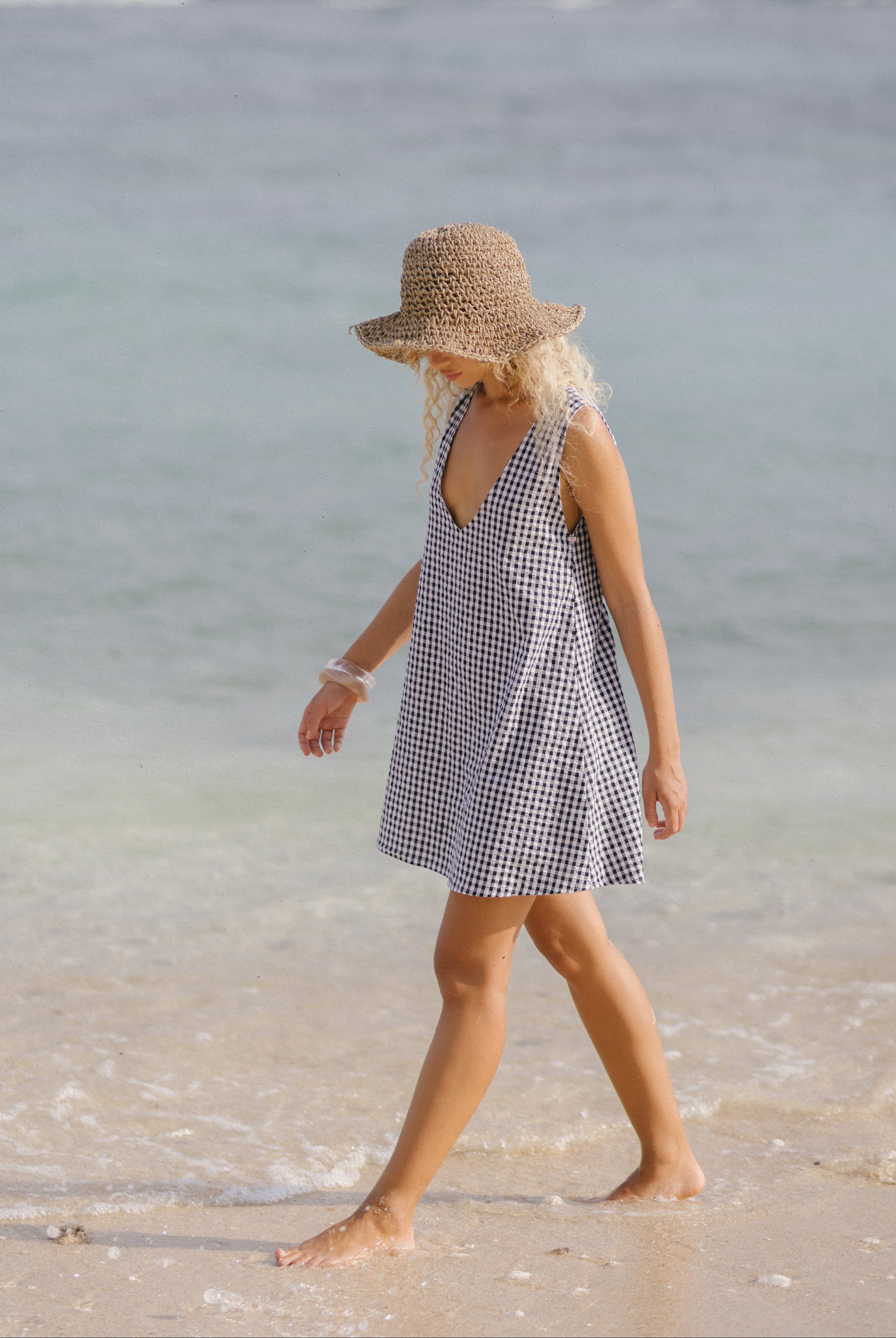 Woman in black gingham mini dress with a v-neck and high neck and a lack of color beach hat