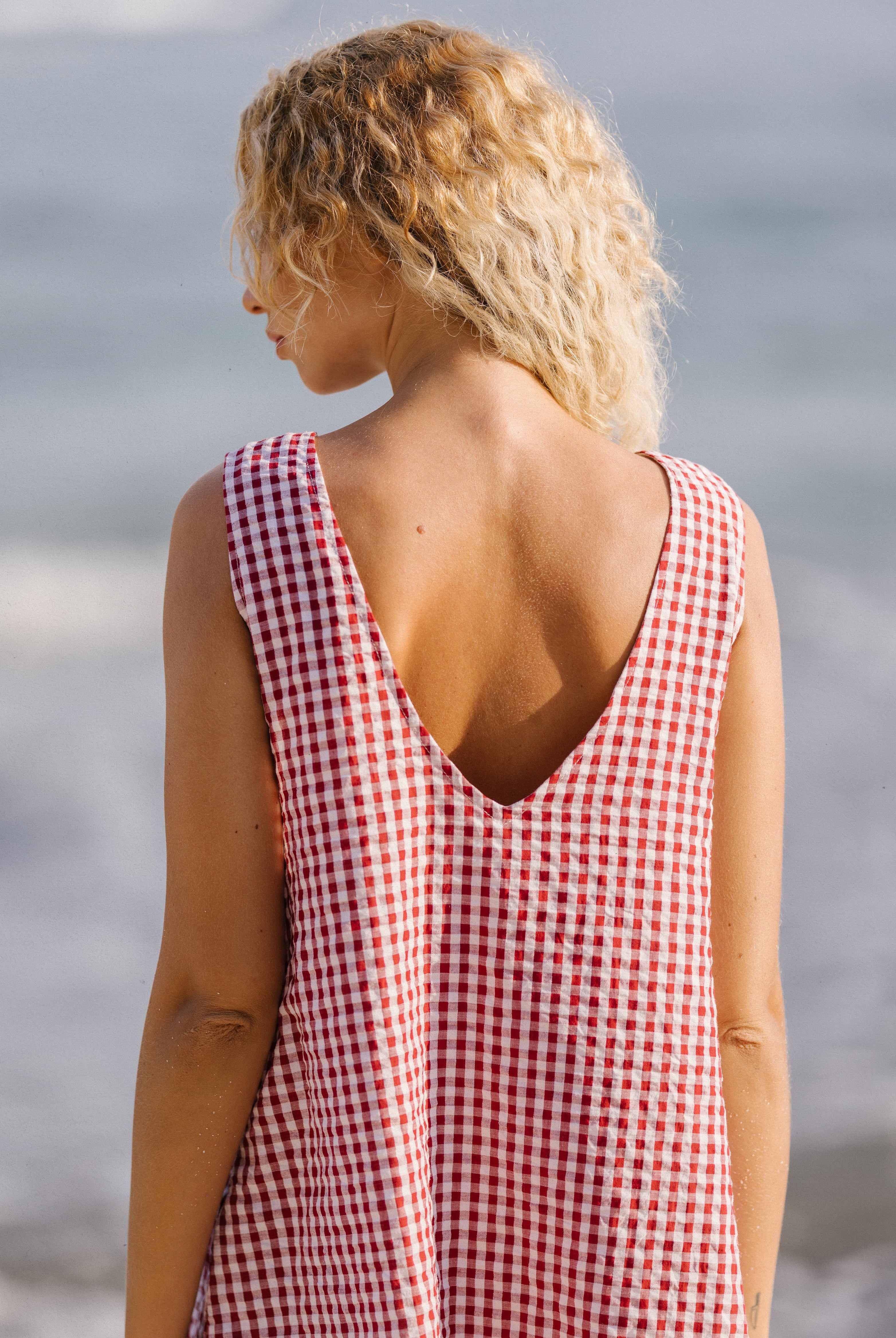 Woman wearing a red and white checkered dress standing by the ocean.