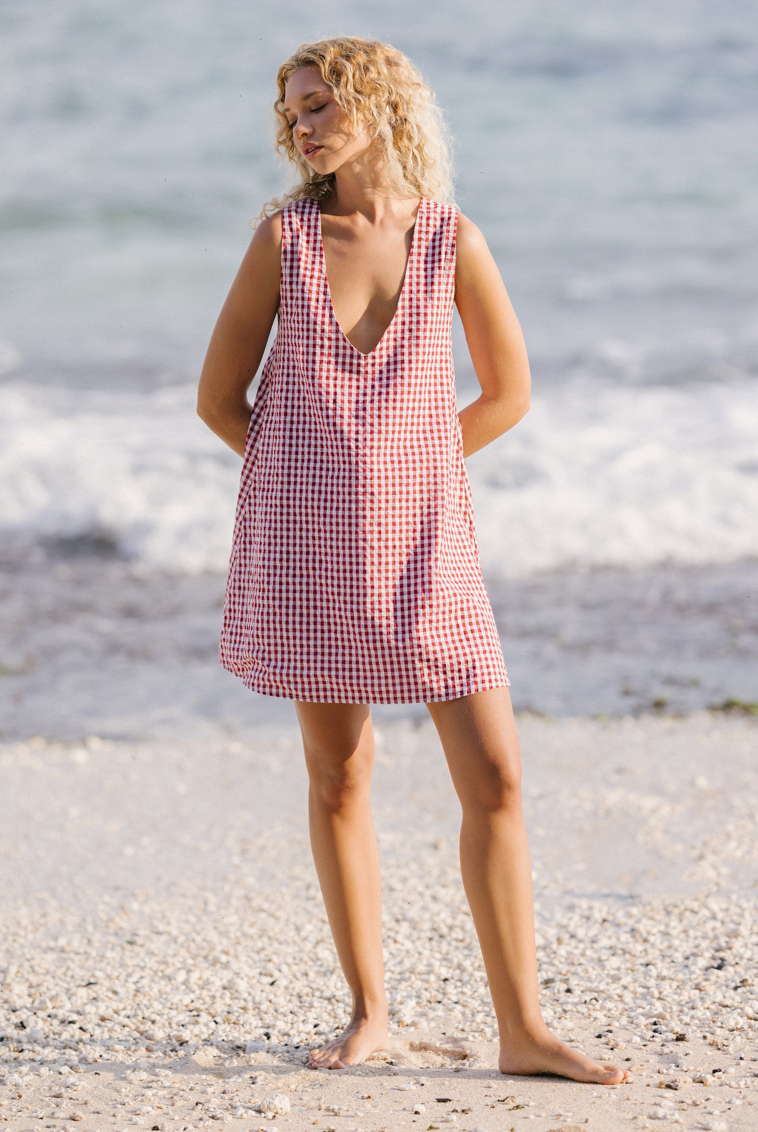 Woman in a red and white checkered dress standing on a beach.