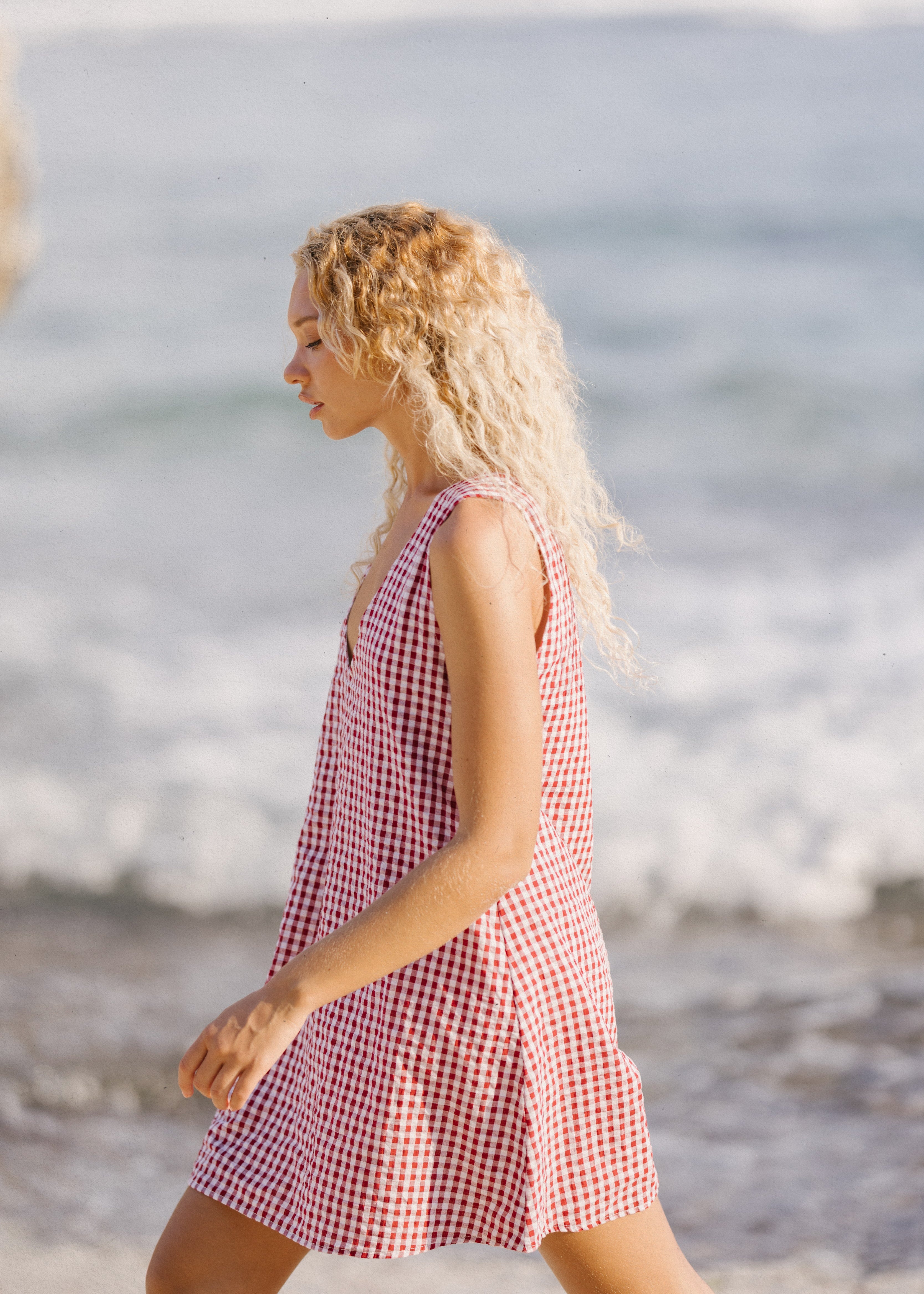 Woman in a red and white checkered dress walking along a beach.
