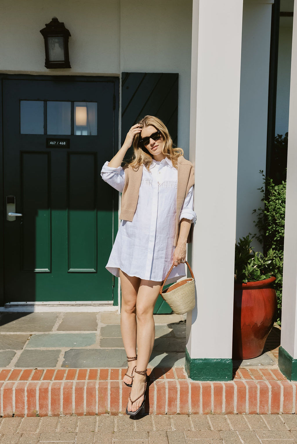 White linen Ulu Dress with black strappy sandals and straw basket bag in front of iconic Montauk Yacht Club green door, MTK summer outfit idea 2026