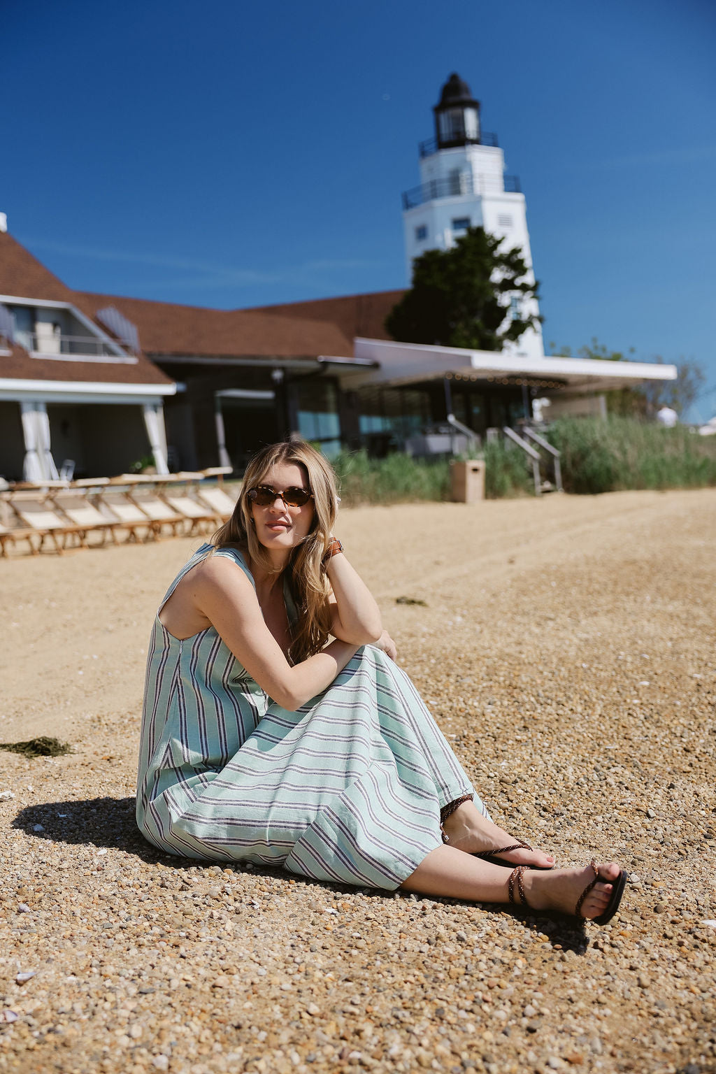 Gili Green Stripe Maxi Dress sitting on pebble beach at Montauk Yacht Club with lighthouse — MTK summer beach dress, Nantucket style stripe maxi dress outfit