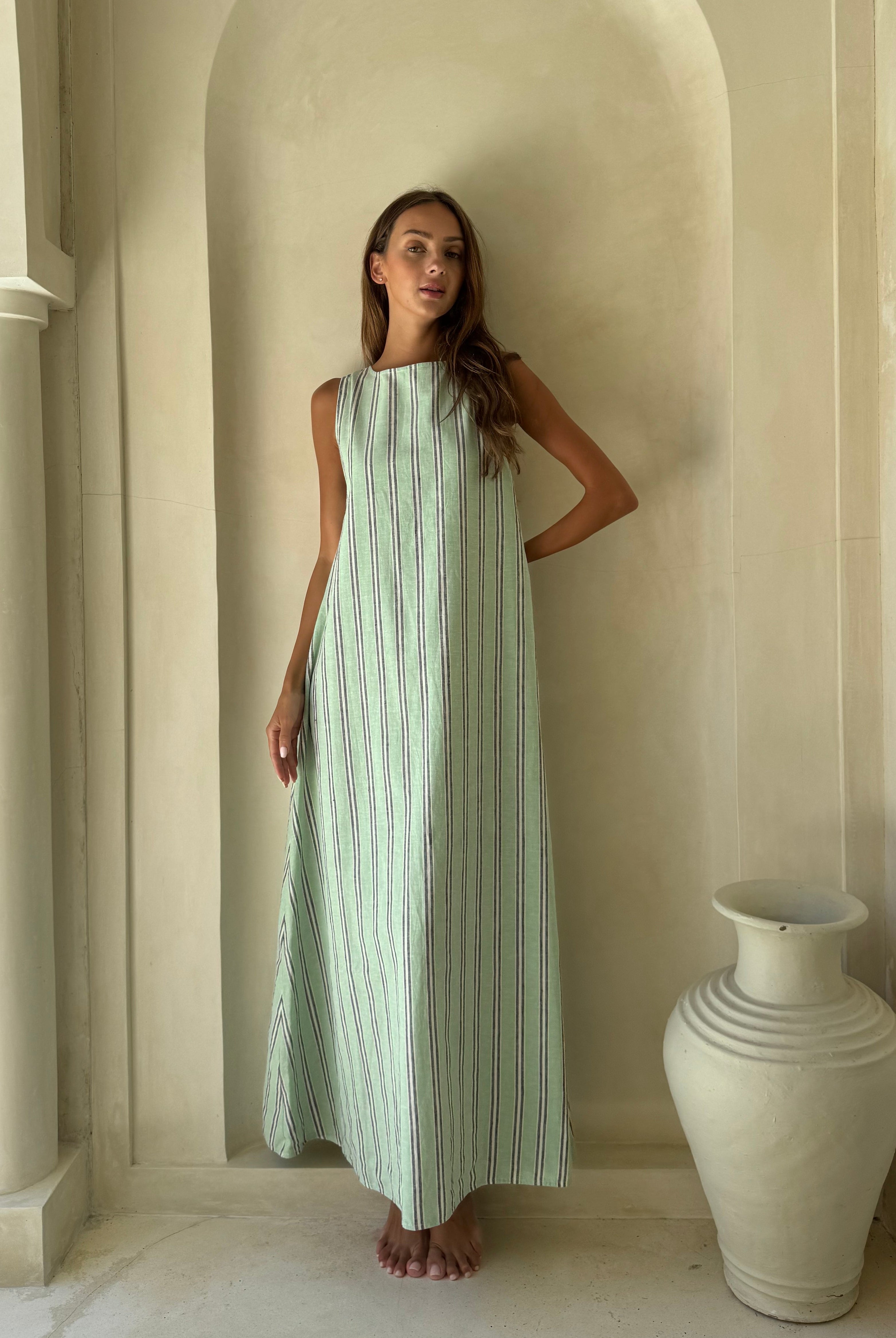 Woman wearing the Gili Green Navy and White Stripe Maxi Dress with high neck styling in front of a stone villa archway