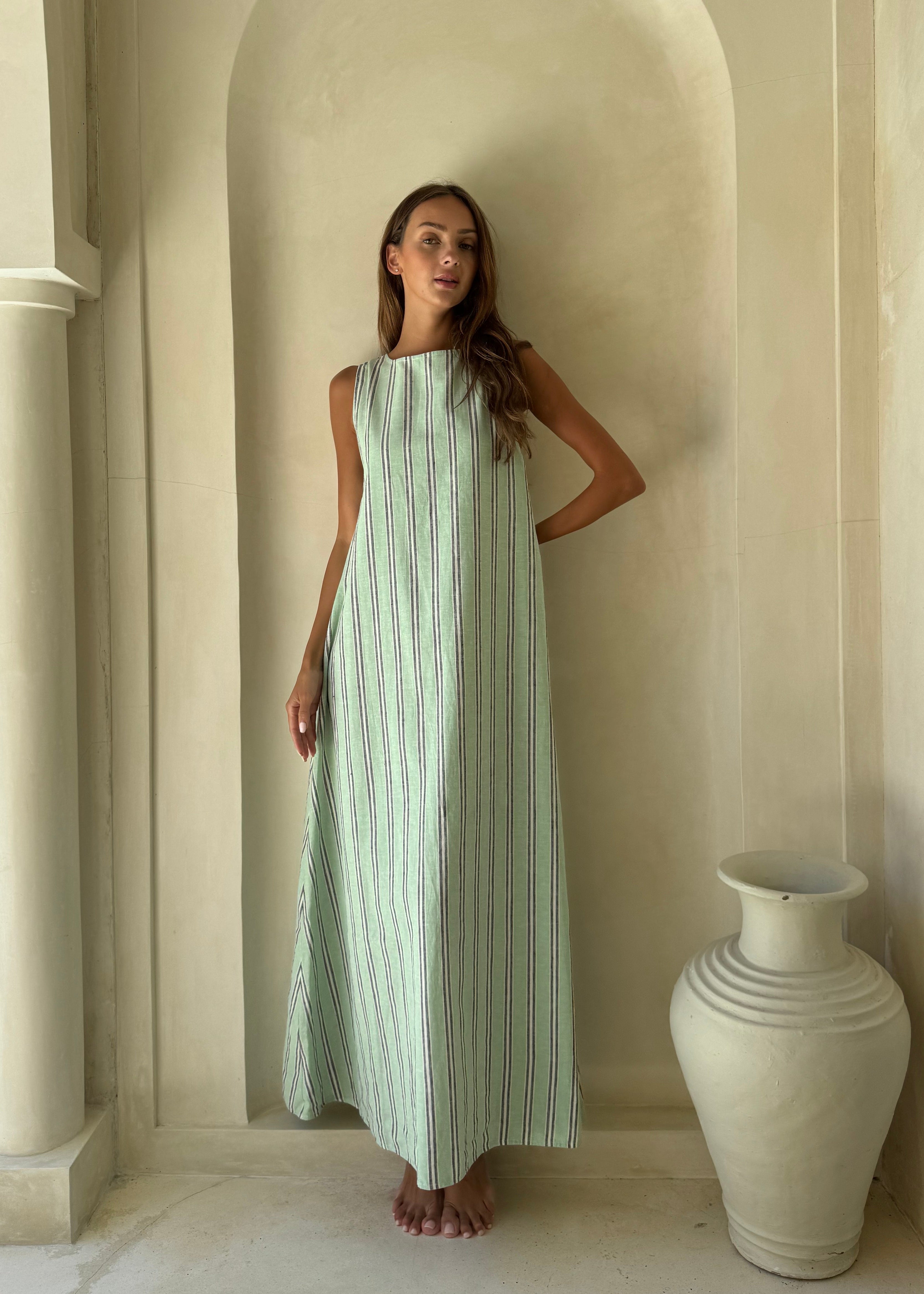 Woman wearing the Gili Green Navy and White Stripe Maxi Dress with high neck styling in front of a stone villa archway