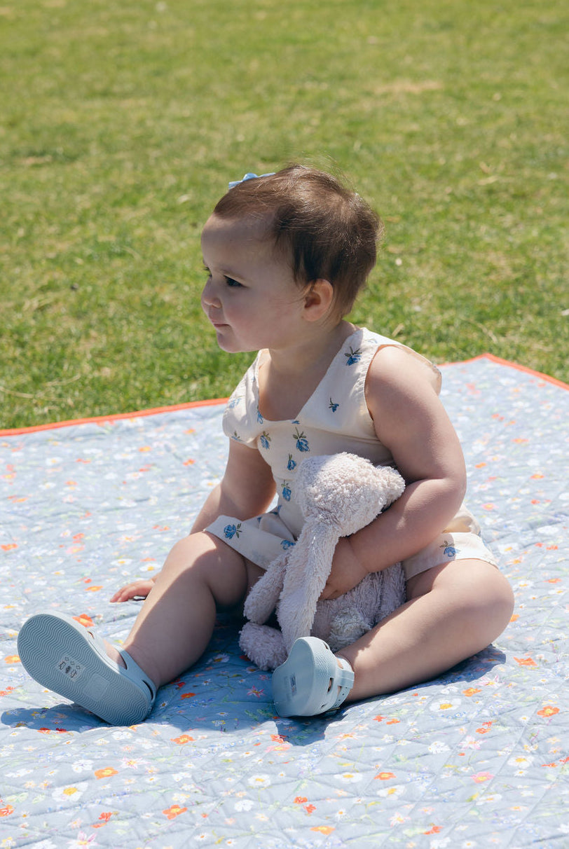 Blue Posey Little Gili baby girl floral cotton dress, toddler sitting on spring picnic blanket with teddy bear Puka The Label