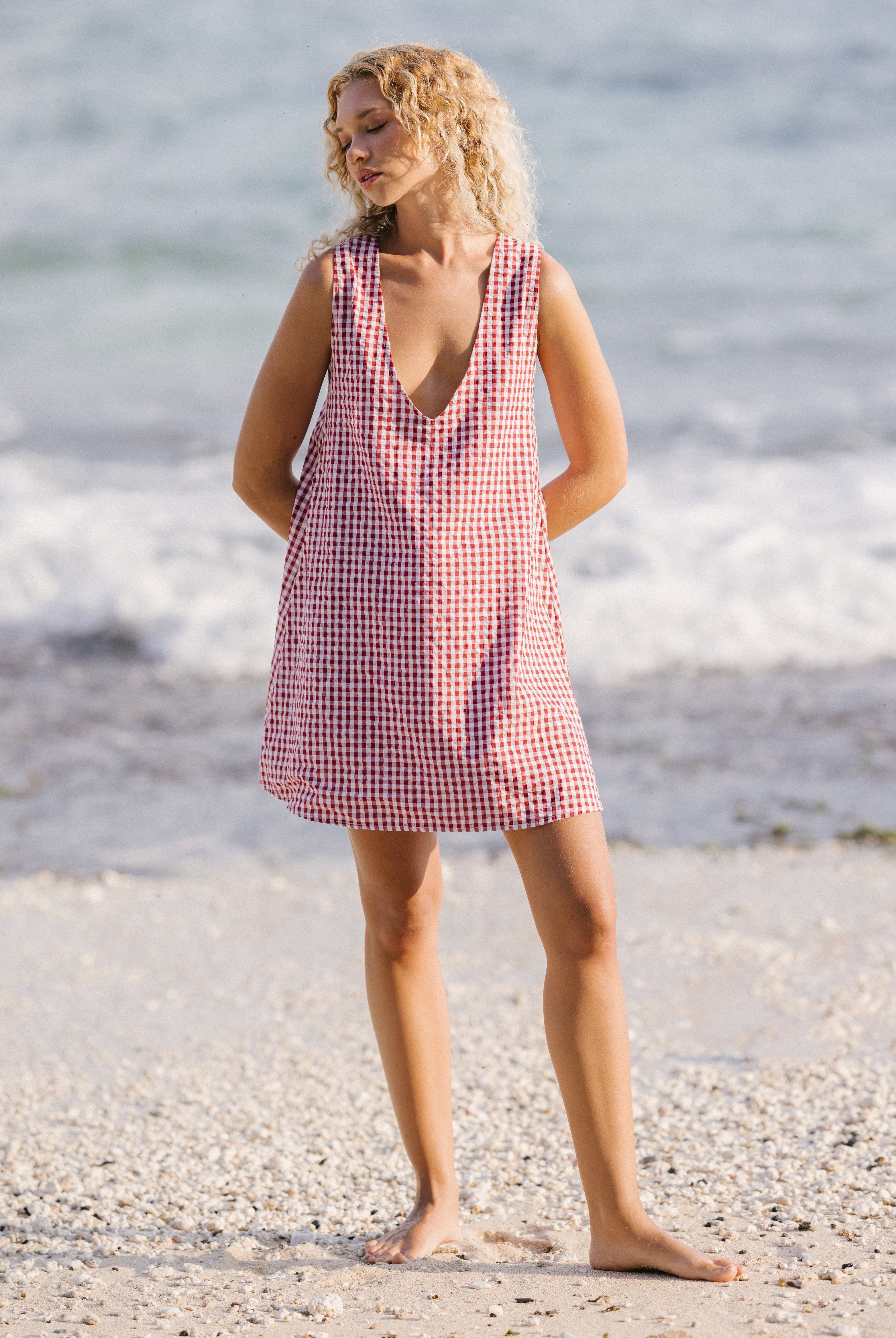 Woman in a red and white checkered dress standing on a beach.