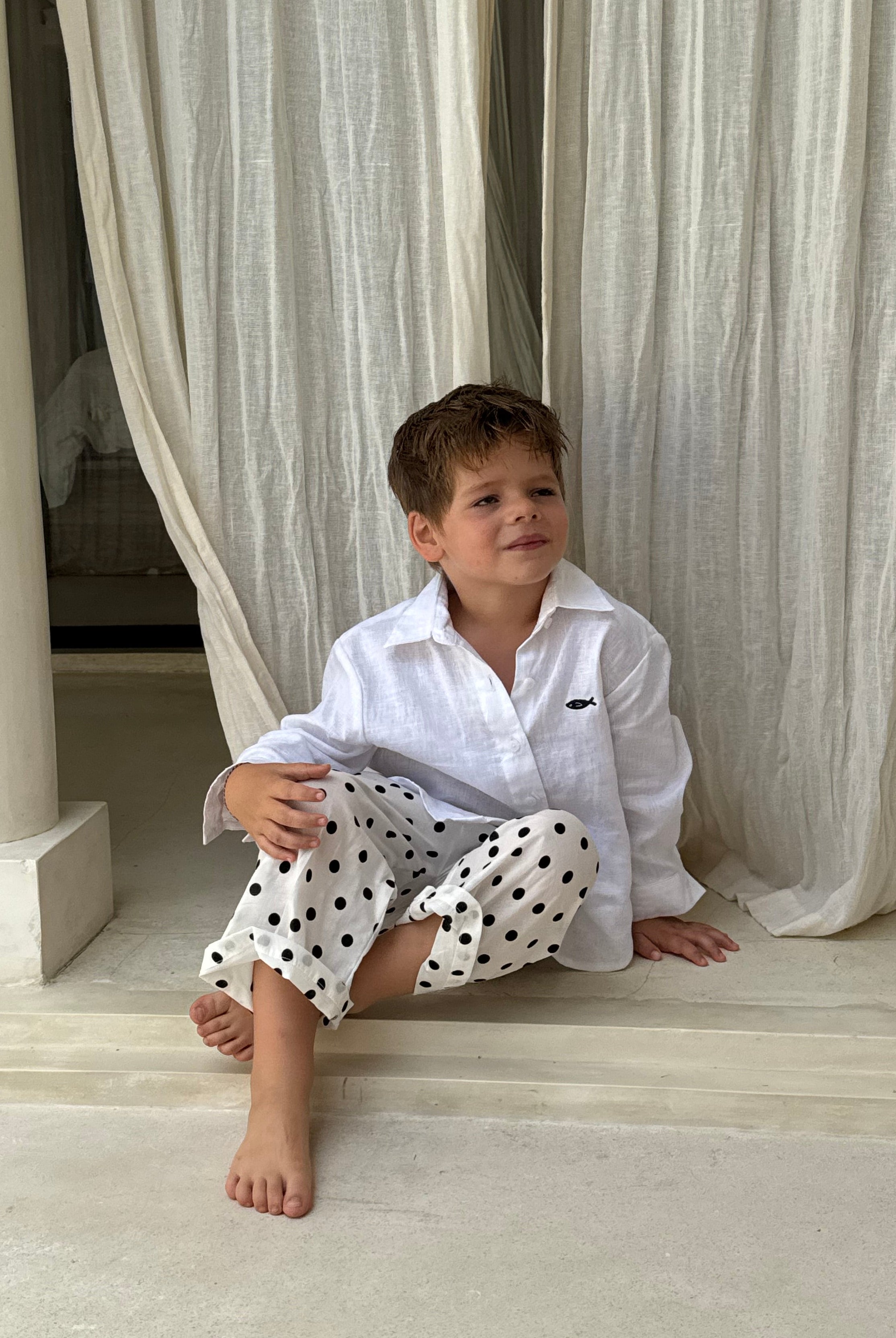 Boy sitting cross-legged in Pantai Polka Dot Pants at a Bali villa, relaxed kids resort wear for beach vacation getaways
