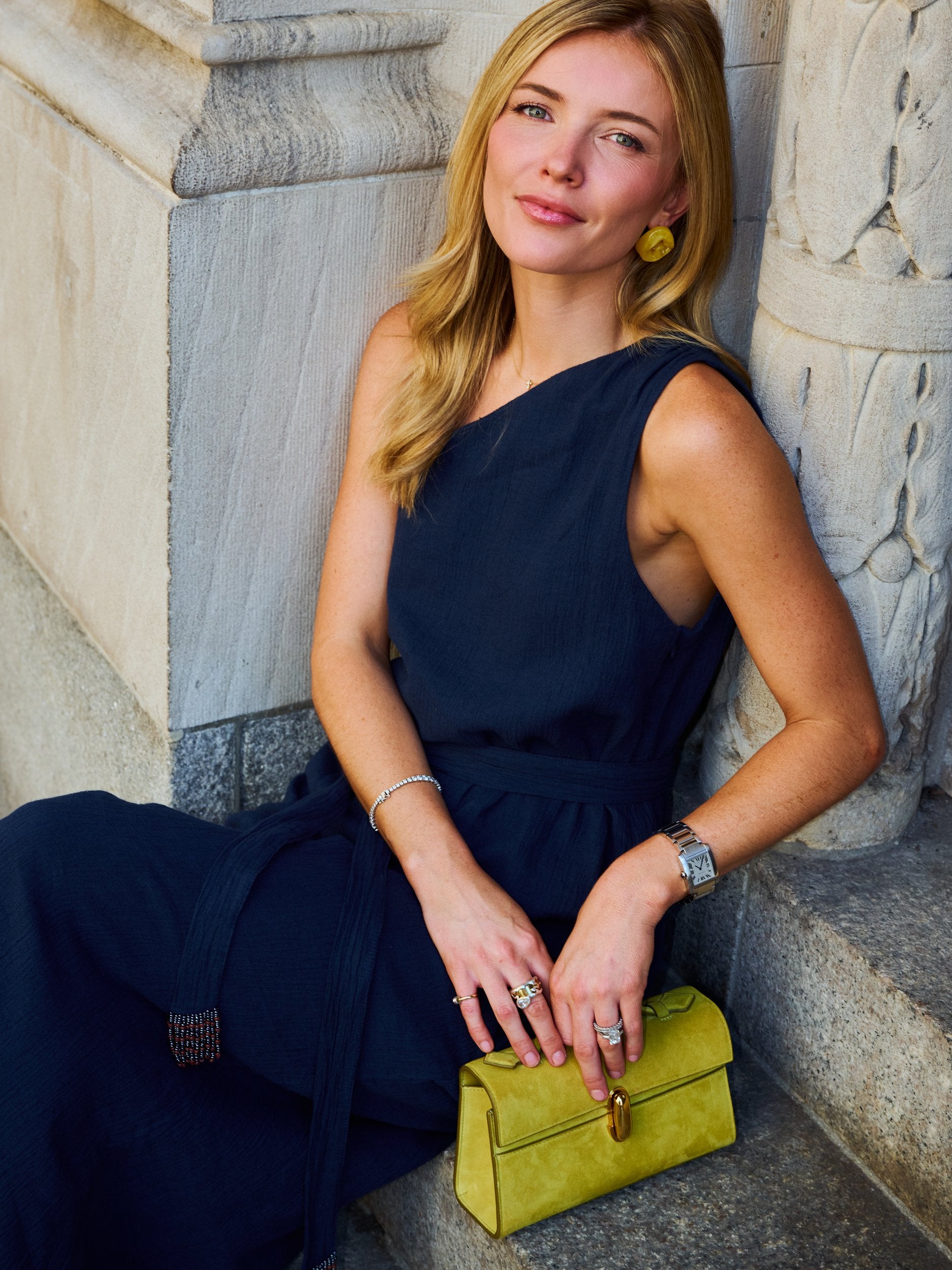 Natalie Simkins wearing Camilla Dress Midnight with olive yellow bag and flower earrings, seated NYC steps