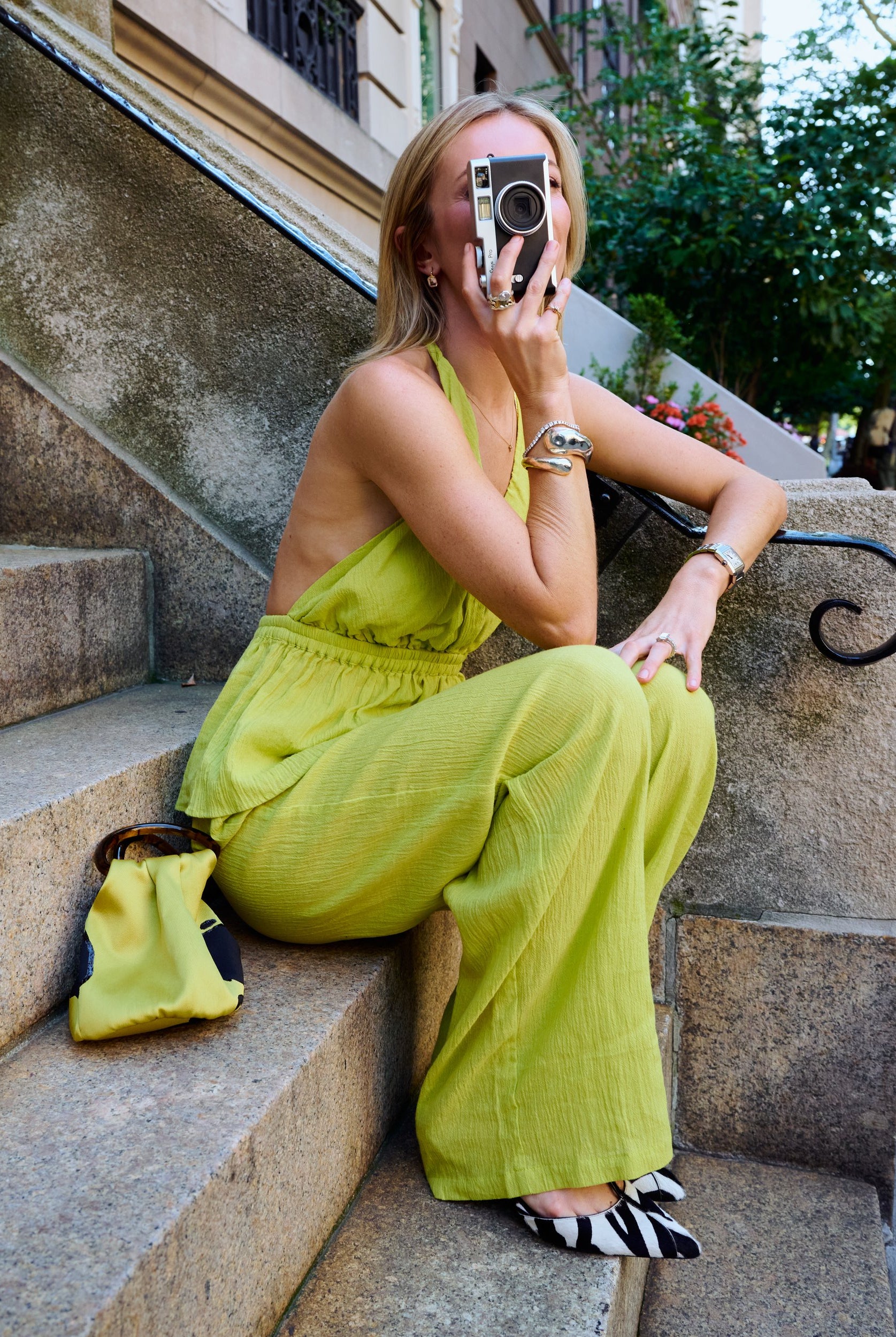 Natalie Simkins in Carlyle Set Olive Brine on NYC brownstone steps holding a film camera, zebra kitten heels