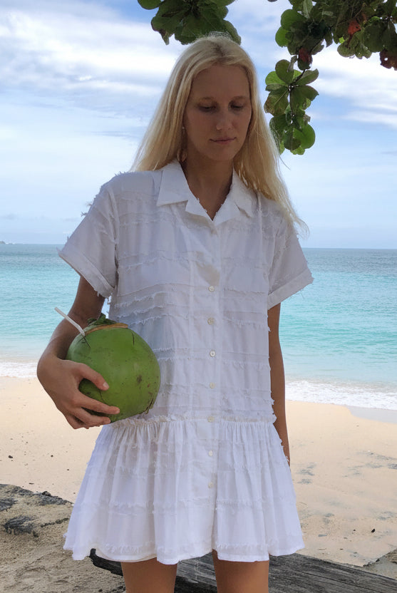 Woman in a white dress holding a coconut on a beach