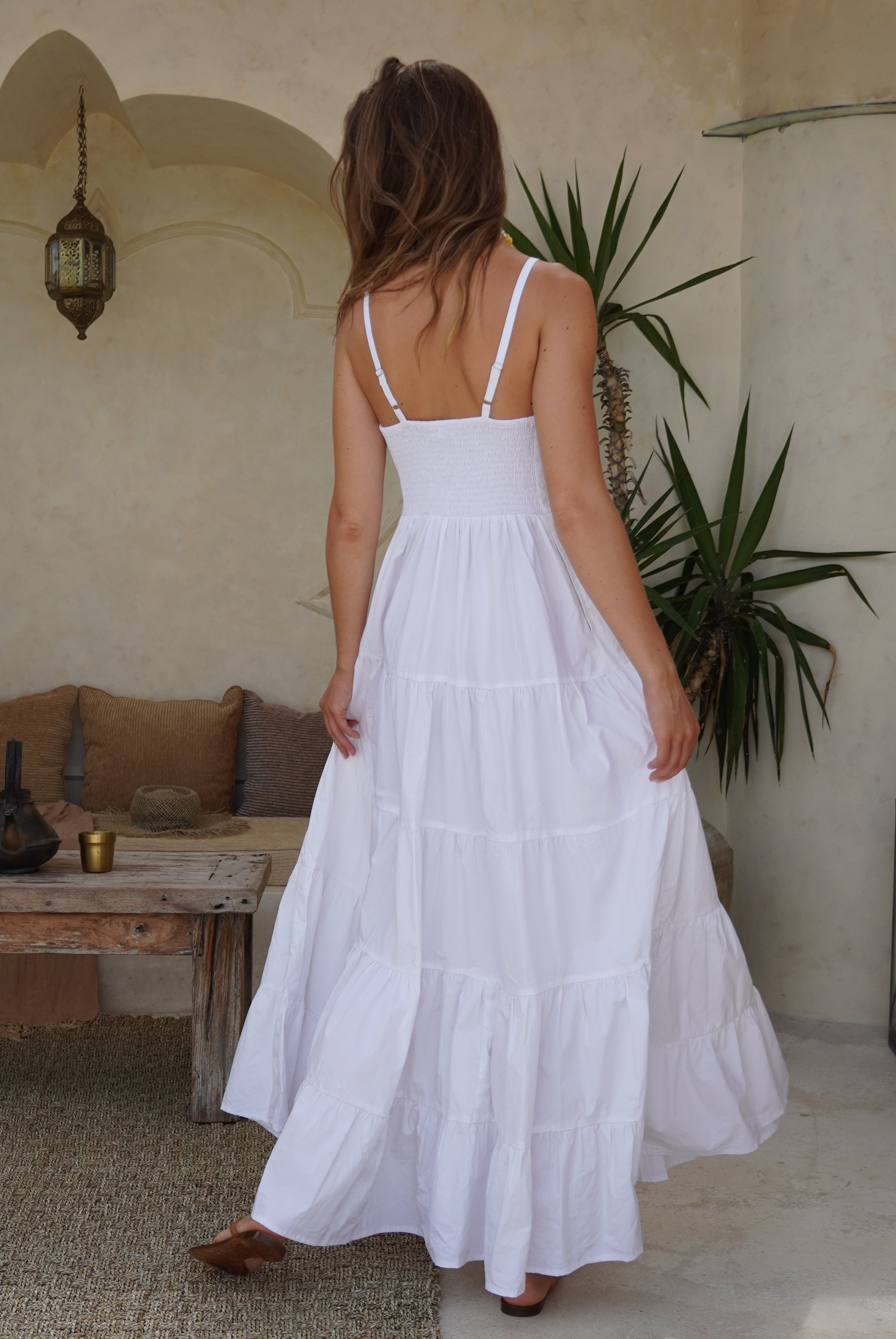 Woman wearing a white dress in an outdoor setting with plants and a table.