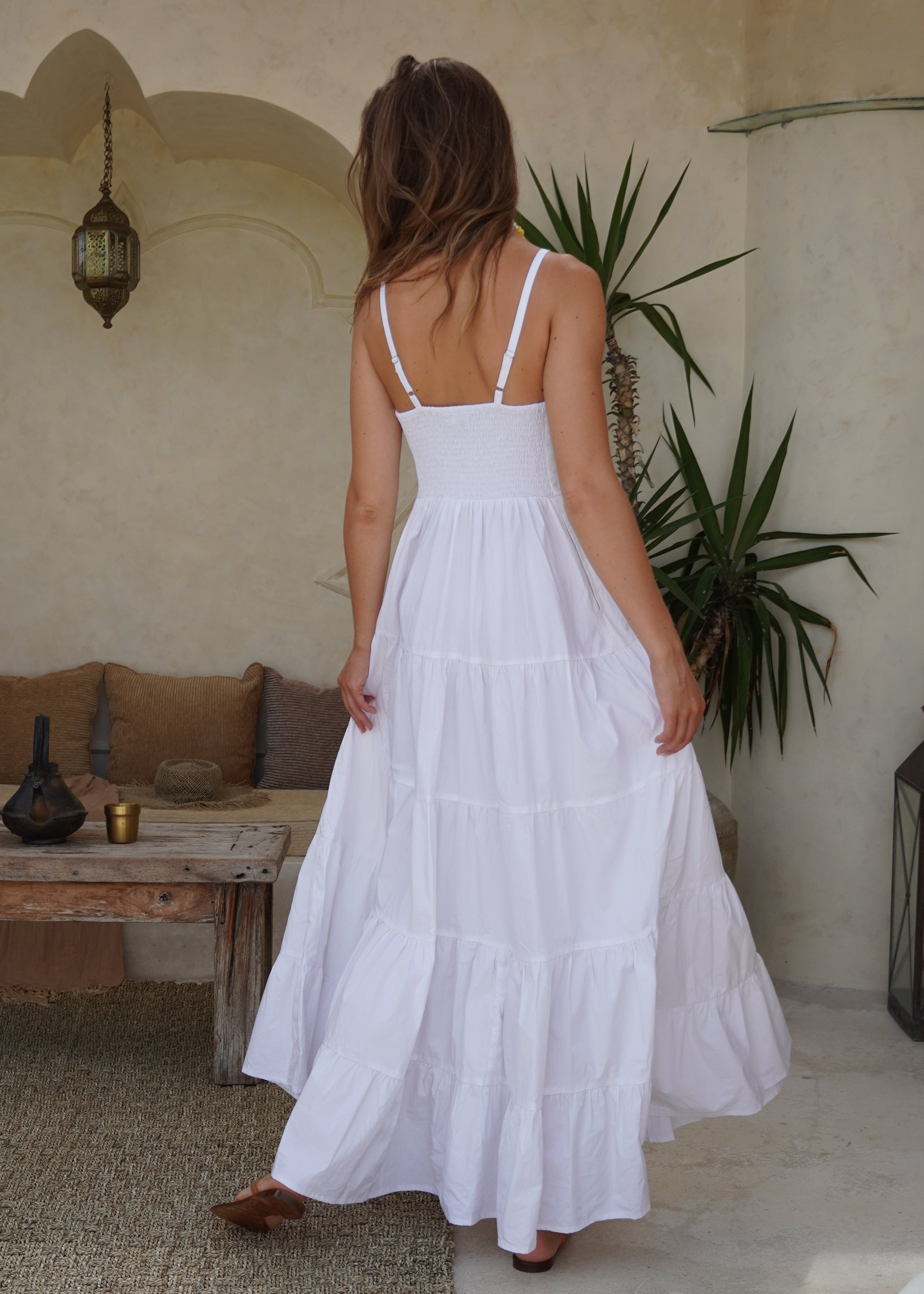 Woman wearing a white dress in an outdoor setting with plants and a table.