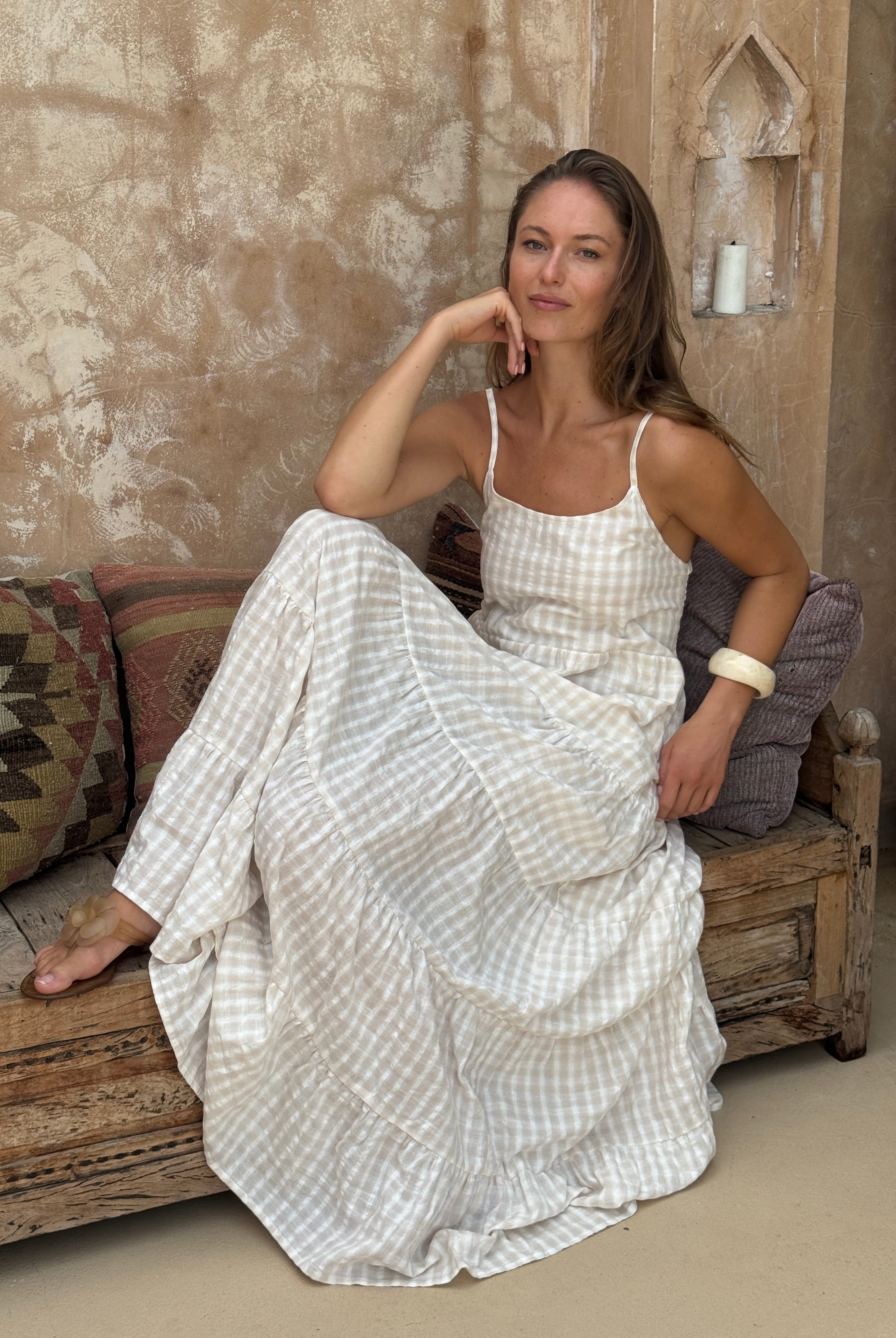 Woman in a white checkered dress lying on a wooden floor with a textured wall and rug in the background.
