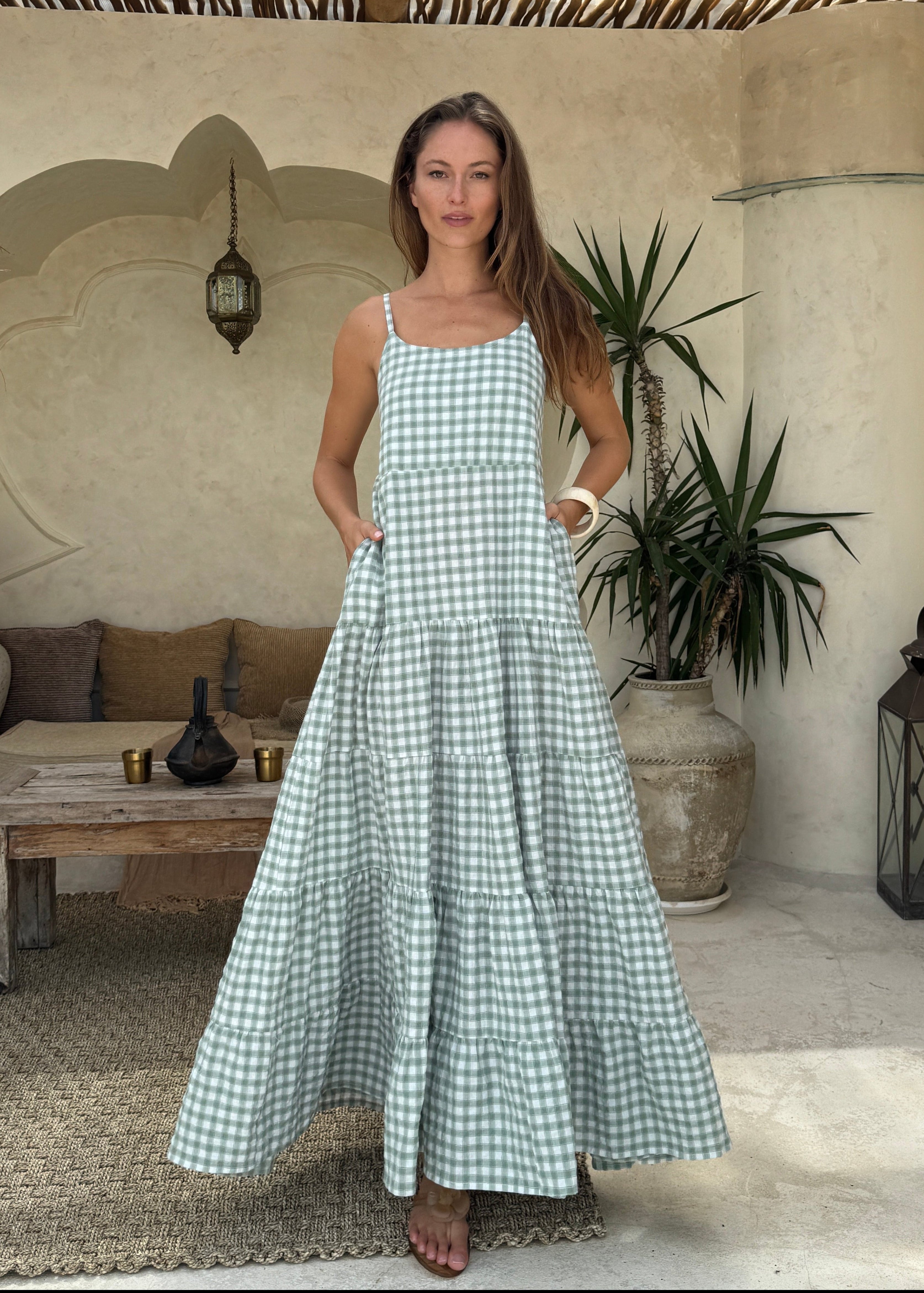 Woman in a green checkered dress standing in a courtyard with plants and lanterns.
