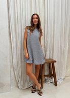 Woman in a checkered dress standing next to a wooden stool against a white curtain backdrop