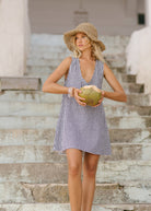 Woman in a black gingham checkered dress and hat holding a coconut on the beach in Bali