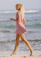 Woman in a red checkered dress walking on a beach with ocean waves in the background