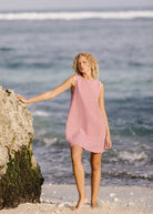 Woman in a red checkered dress standing on a beach with ocean waves in the background