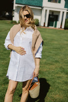 White linen hand-beaded fringe Ulu Dress with camel cardigan draped over shoulders at Montauk Yacht Club, East Hampton Hamptons summer outfit 2026