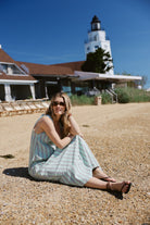 Gili Green Stripe Maxi Dress sitting on pebble beach at Montauk Yacht Club with lighthouse — MTK summer beach dress, Nantucket style stripe maxi dress outfit