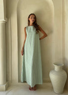 Woman wearing the Gili Green Navy and White Stripe Maxi Dress with high neck styling in front of a stone villa archway