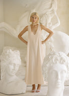 Woman in a beige dress standing among white sculptures of heads.