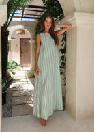 Gili Green Navy and White Stripe Maxi Dress with low V-neck styling in a tropical resort archway, barefoot beach vacation look