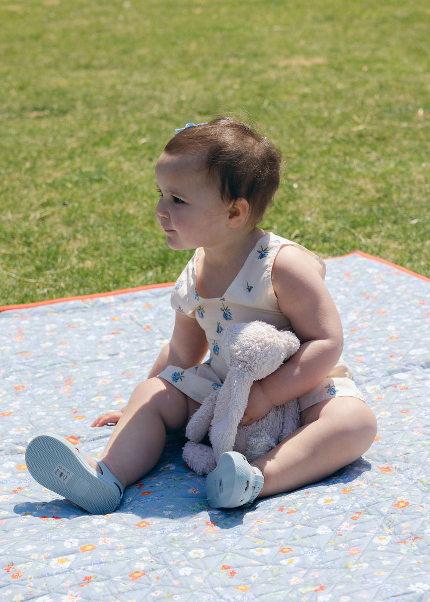 Blue Posey Little Gili baby girl floral cotton dress, toddler sitting on spring picnic blanket with teddy bear Puka The Label