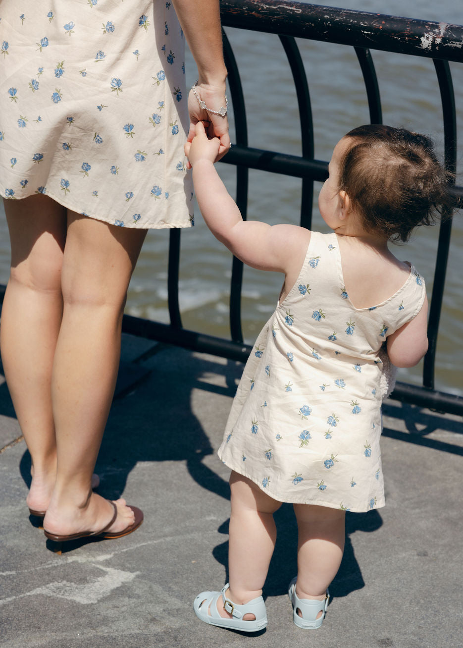 Blue Posey Little Gili toddler dress close view, baby girl in blue floral cotton dress reaching for mom at waterfront railing Puka The Label