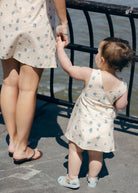 Blue Posey Little Gili toddler dress close view, baby girl in blue floral cotton dress reaching for mom at waterfront railing Puka The Label
