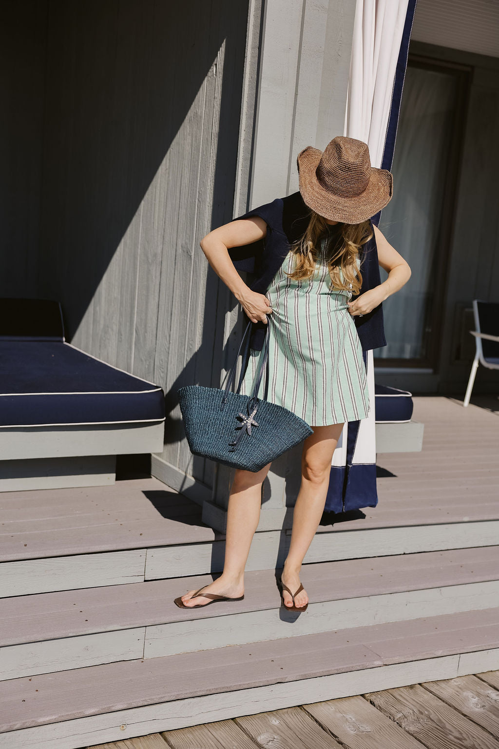 Mini Gili aquamarine stripe hemp cotton dress with raffia hat and navy woven tote on Montauk Yacht Club pool deck, Hamptons summer outfit idea 2026 Puka The Label