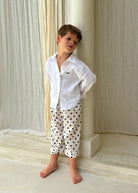 Boy wearing Pantai Polka Dot Pants with a white linen shirt, standing barefoot in a Bali resort villa — kids beach vacation outfit