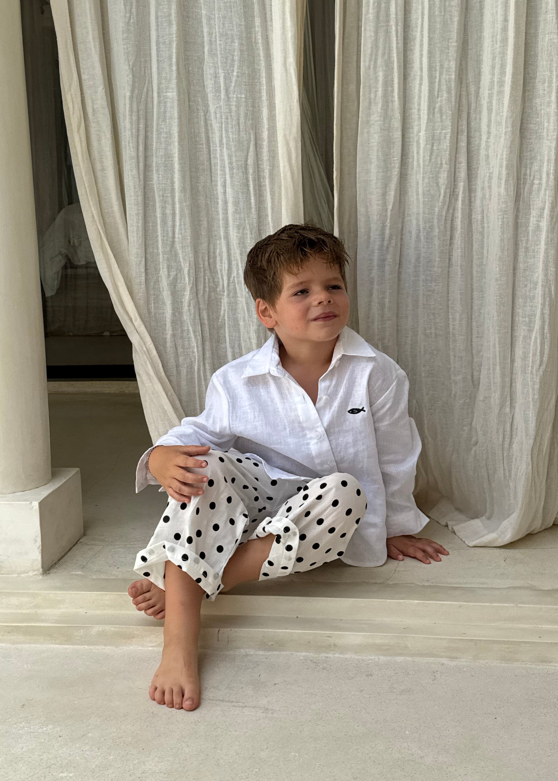 Boy sitting cross-legged in Pantai Polka Dot Pants at a Bali villa, relaxed kids resort wear for beach vacation getaways