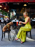 Natalie Simkins in olive brine Carlyle Set at NYC sidewalk cafe reaching for a croissant, her dog beside her
