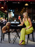 Natalie Simkins in Carlyle Set Olive Brine seated at NYC cafe holding coffee, curly dog on chair