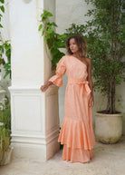 Woman in a peach dress standing in front of a white door with greenery around.