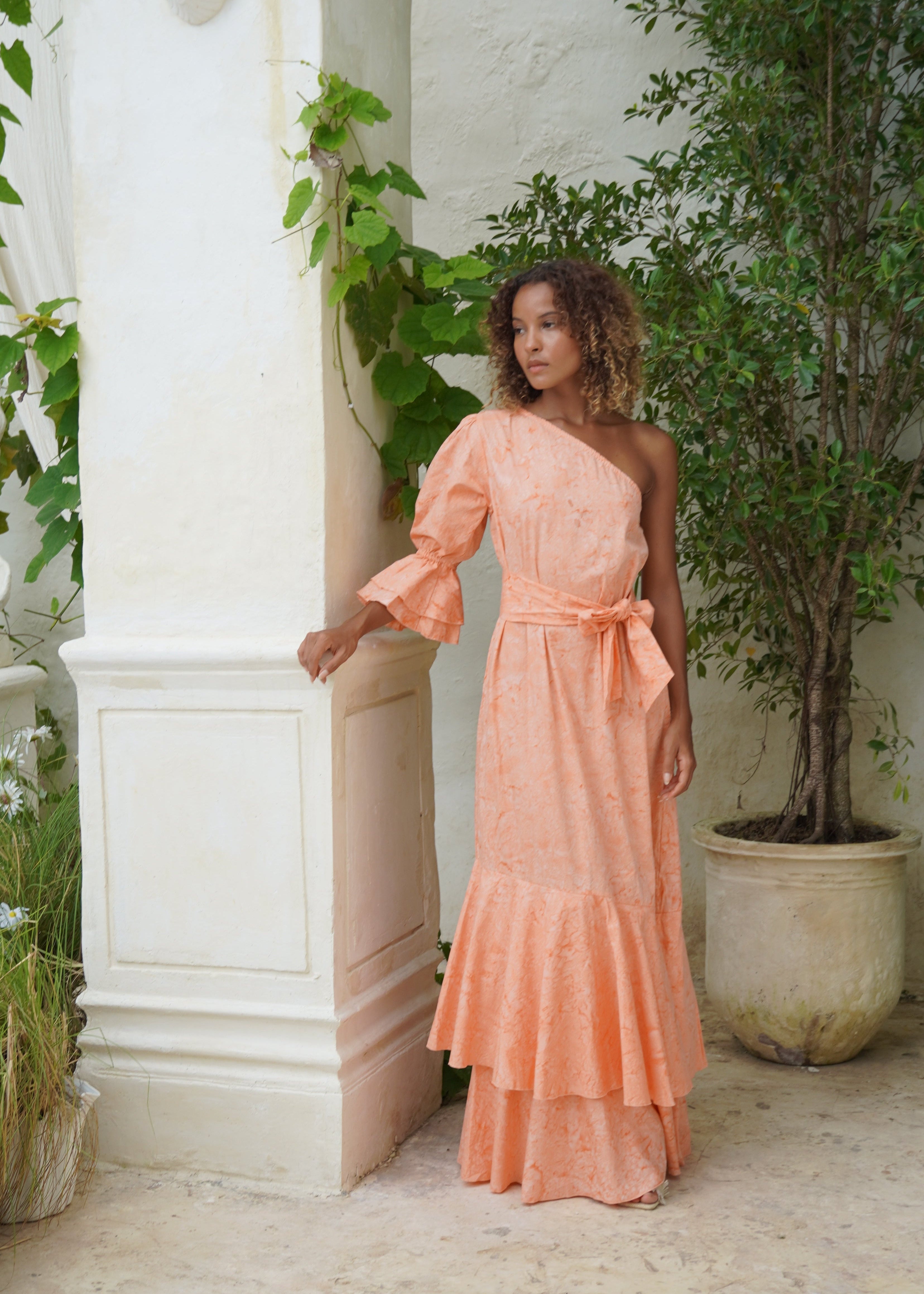 Woman in a peach dress standing in front of a white door with greenery around.