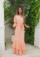 Woman in a peach ruffle dress standing in front of a white wall with greenery