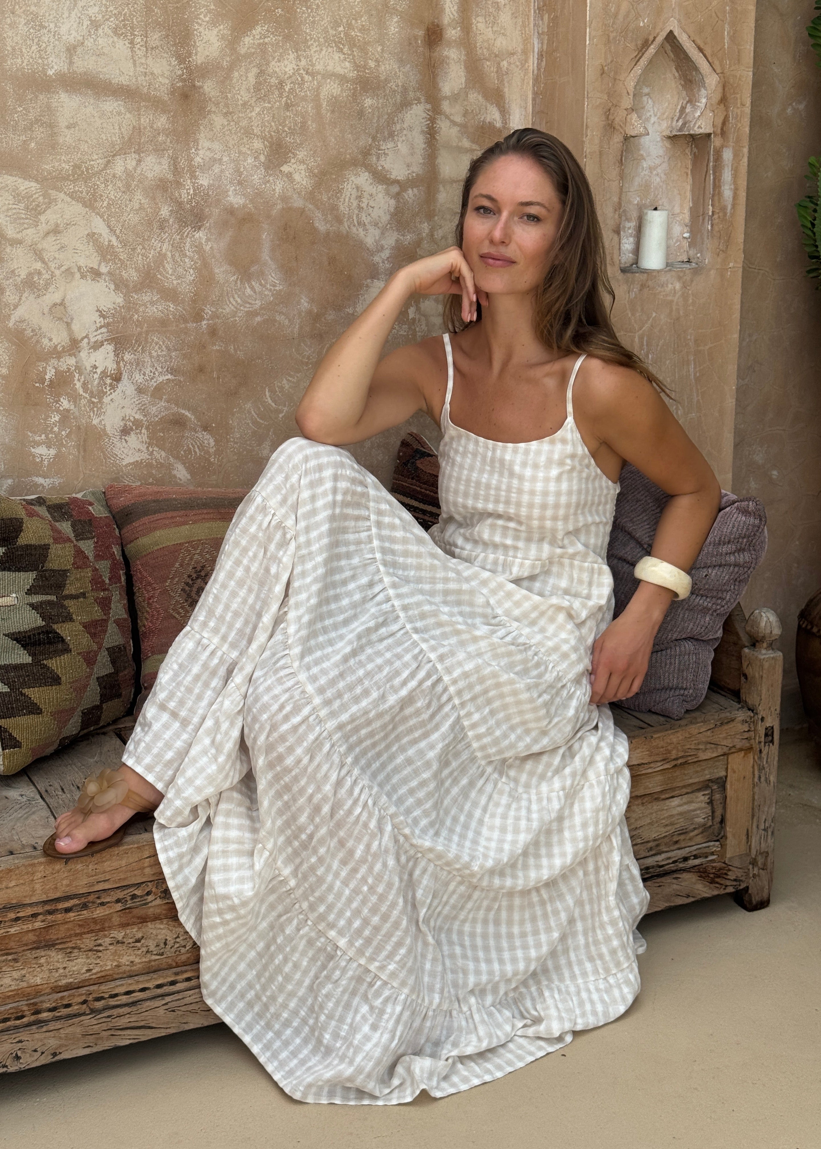 Woman in a white checkered dress lying on a wooden floor with a textured wall and rug in the background.