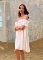 Woman in a white dress standing in a sandy area with a textured wall in the background
